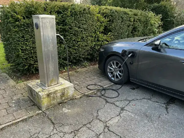 Laadpaal aan de gevel van een woning met een wagen op de oprit